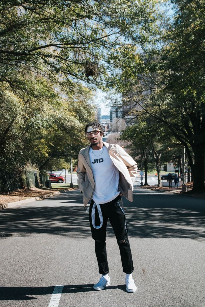 Young adult man posing stylishly on a tree-lined street in urban setting.