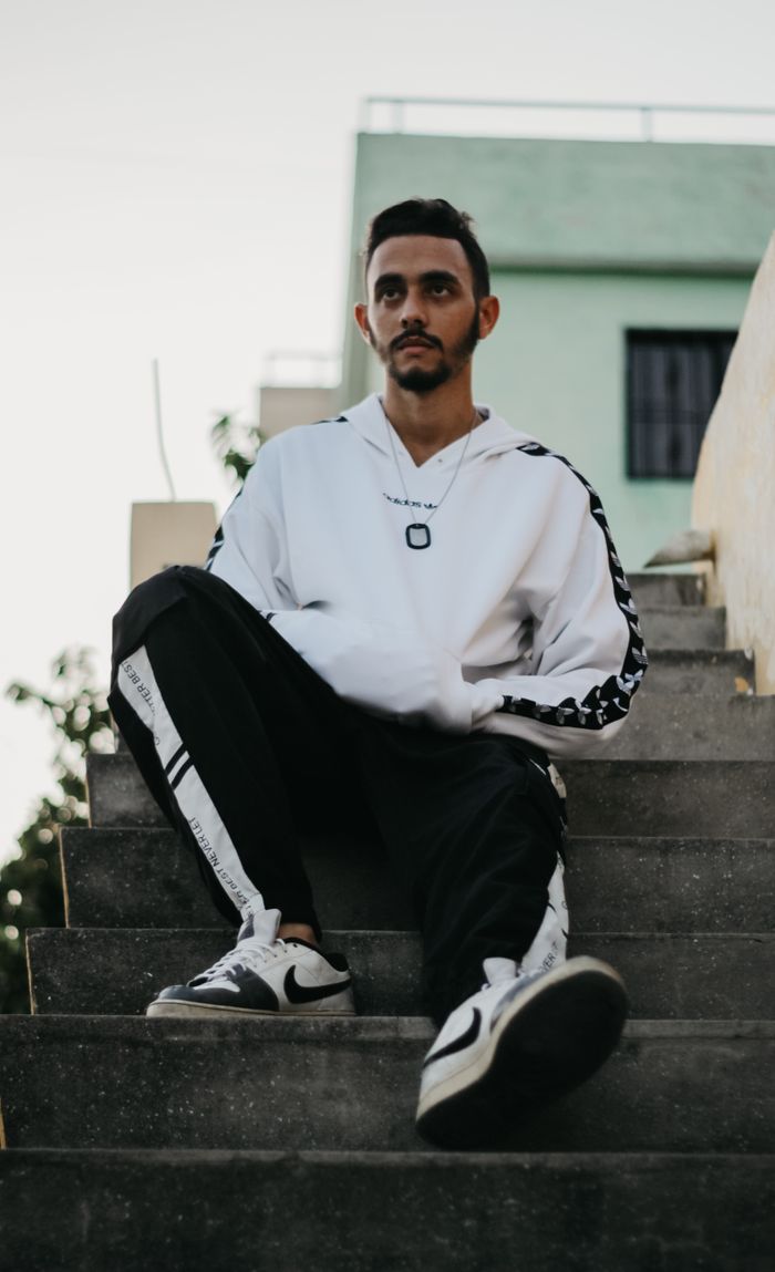 A stylish young man wearing streetwear sits on steps outdoors, embodying modern urban fashion.